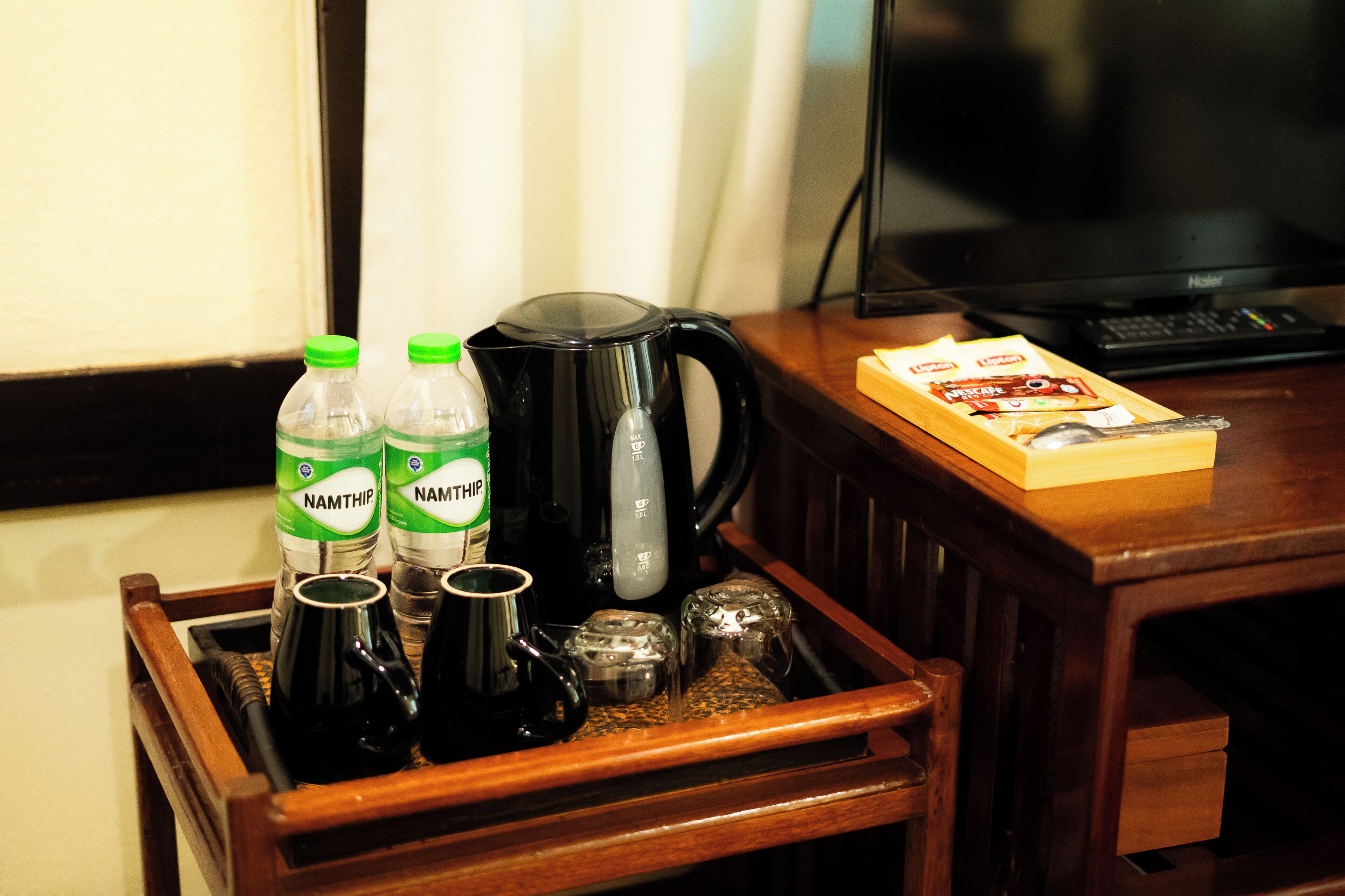 A tray with bottles, a coffee pot, salt and pepper shakers, a box of tissues, and a laptop on a wooden table.