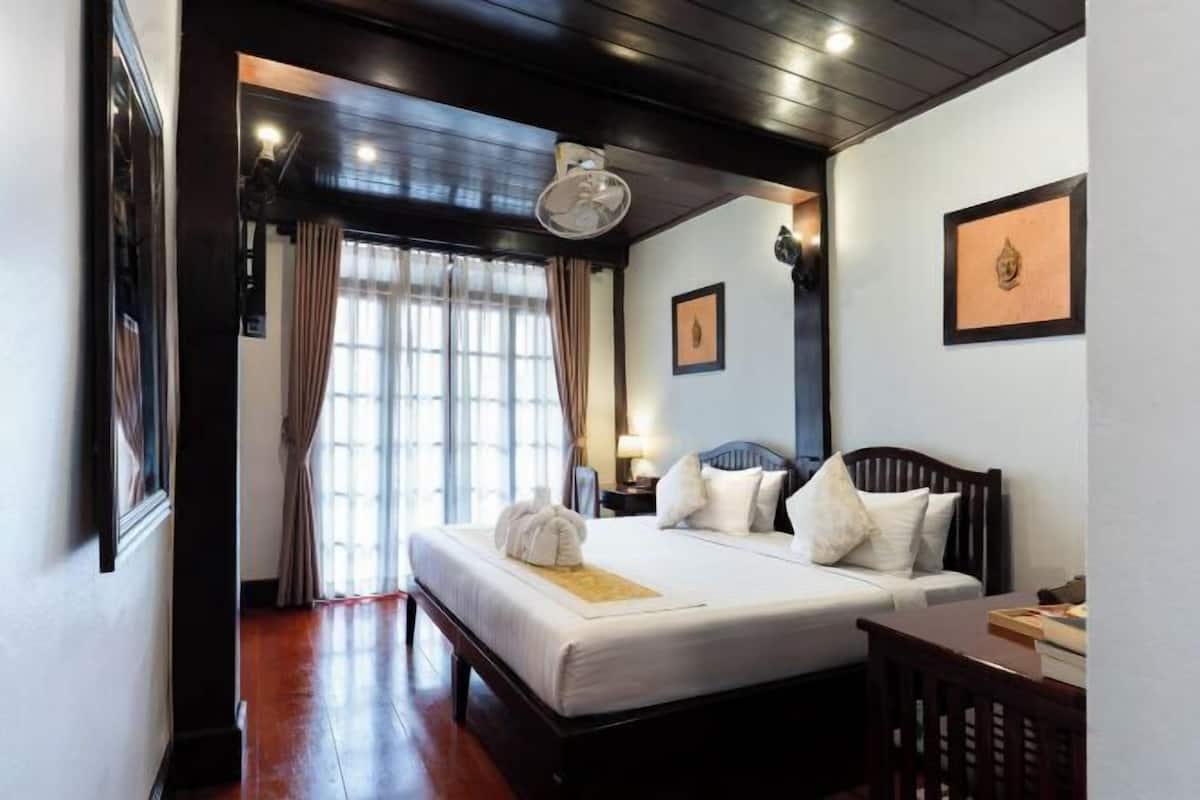 A hotel room with a bed, bedside table, lamp, and a view of the outside through the window.