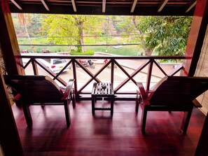 Una terraza de madera con dos sillas y un banco, con vista a un área verde con árboles y un cuerpo de agua.
