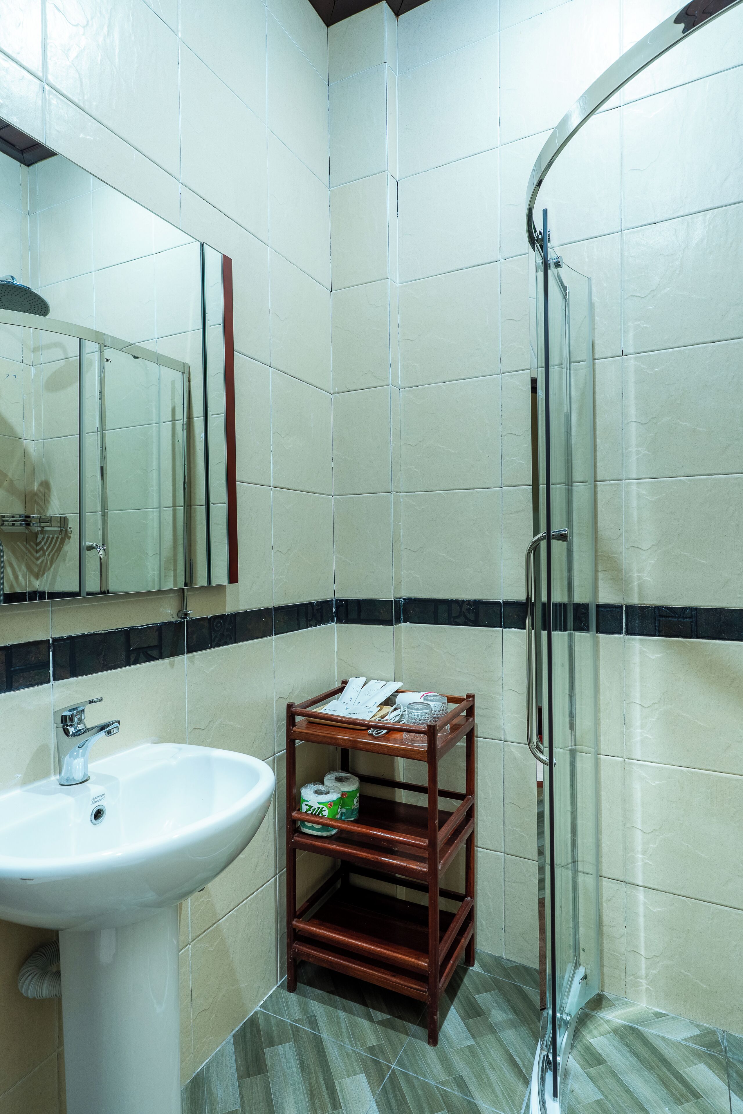 Baño con lavamanos, espejo, ducha y repisa de madera con artículos de aseo.