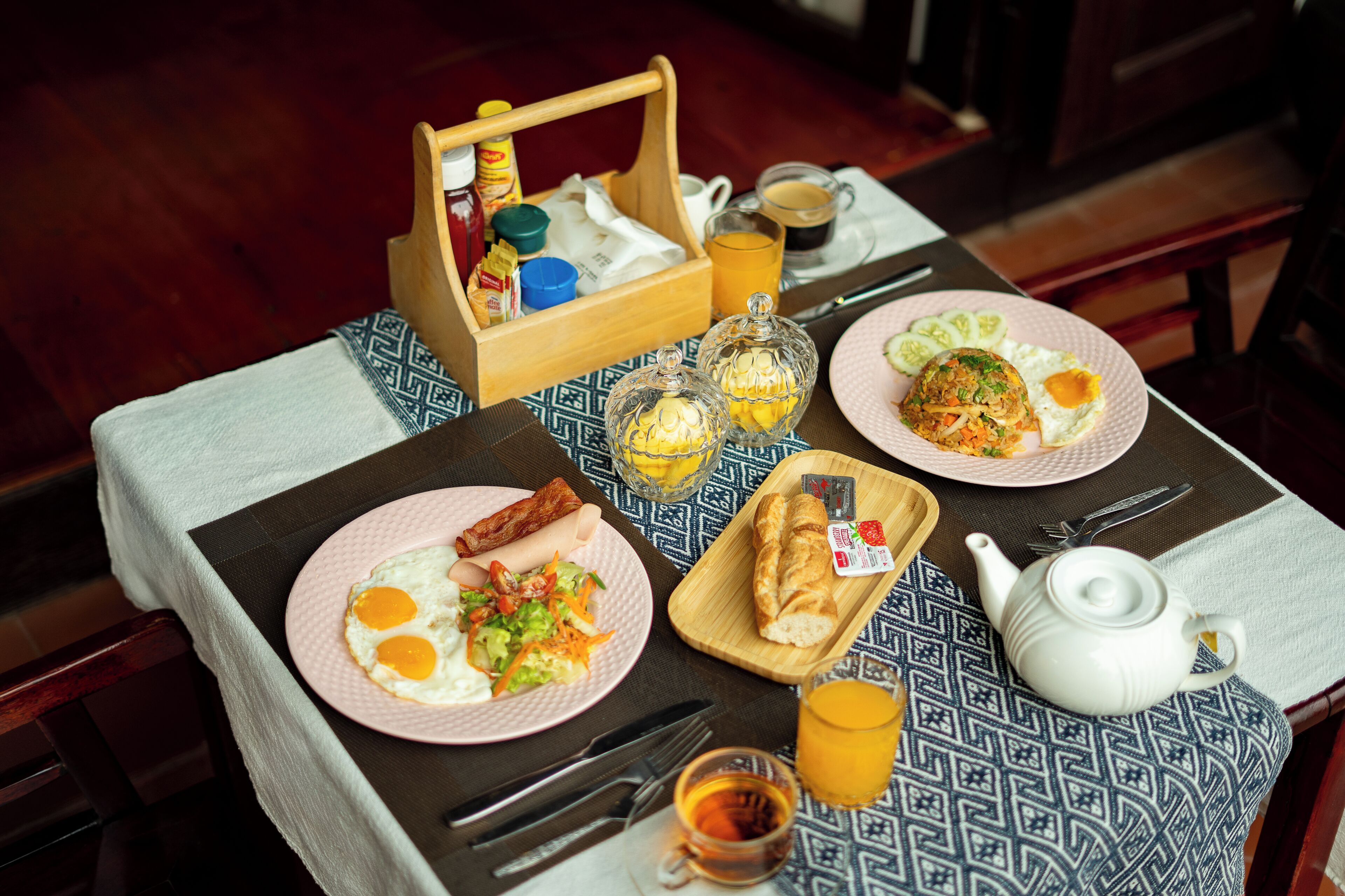 A breakfast table with plates of food, a teapot, and a fruit basket.