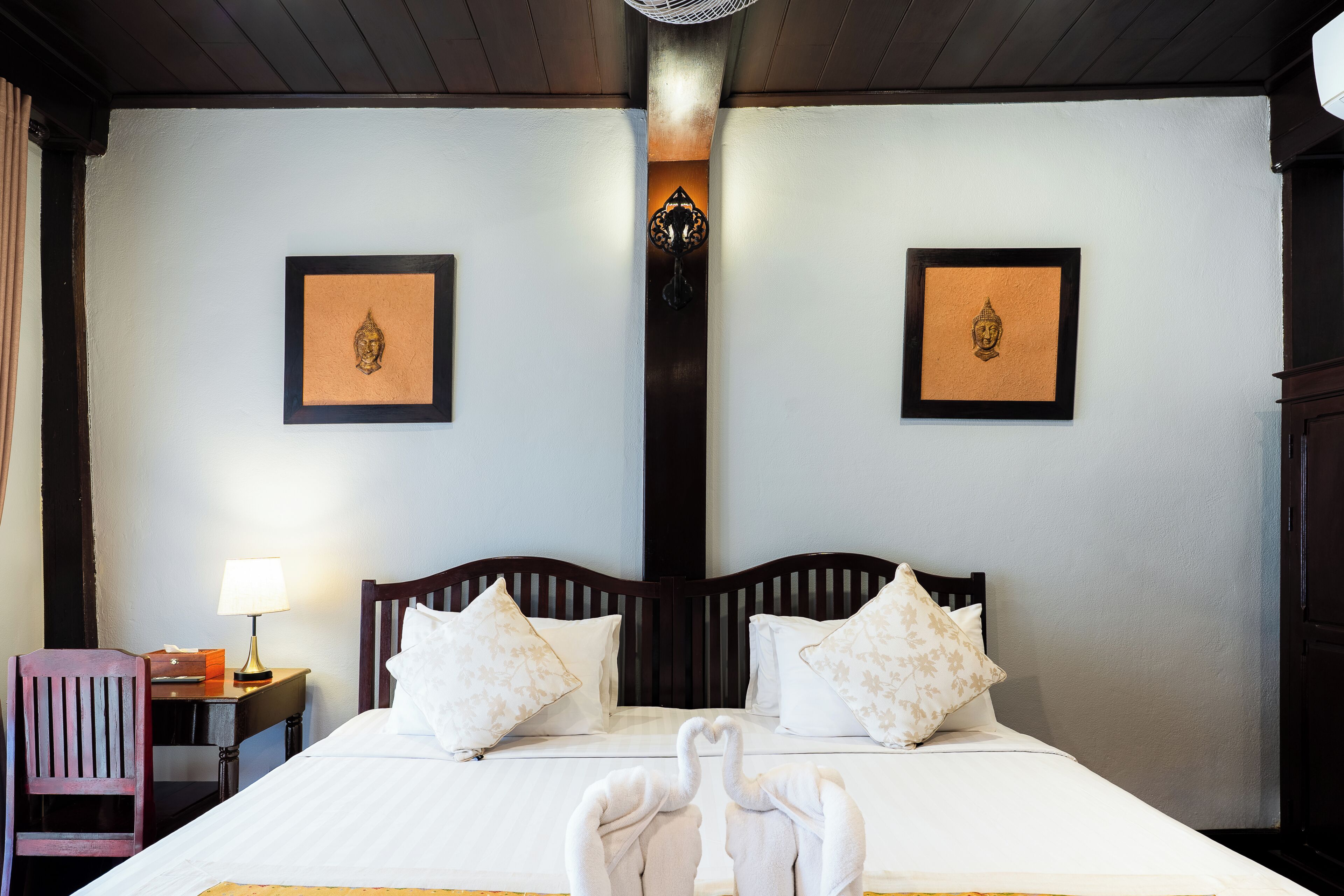 A hotel room with a bed, two pillows, a nightstand with a lamp, a chair, and two framed pictures on the wall.