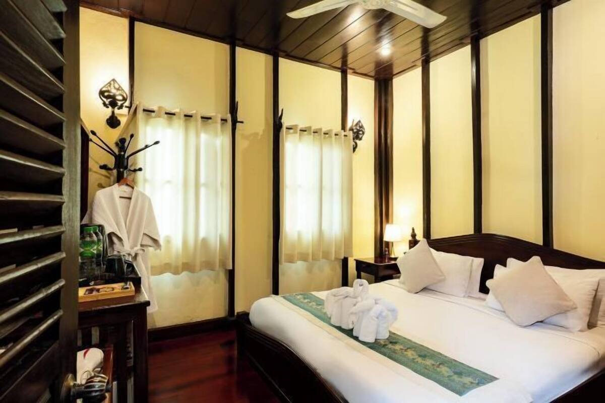 A hotel room with a bed, a nightstand, a lamp, a ceiling fan, and a window with curtains.