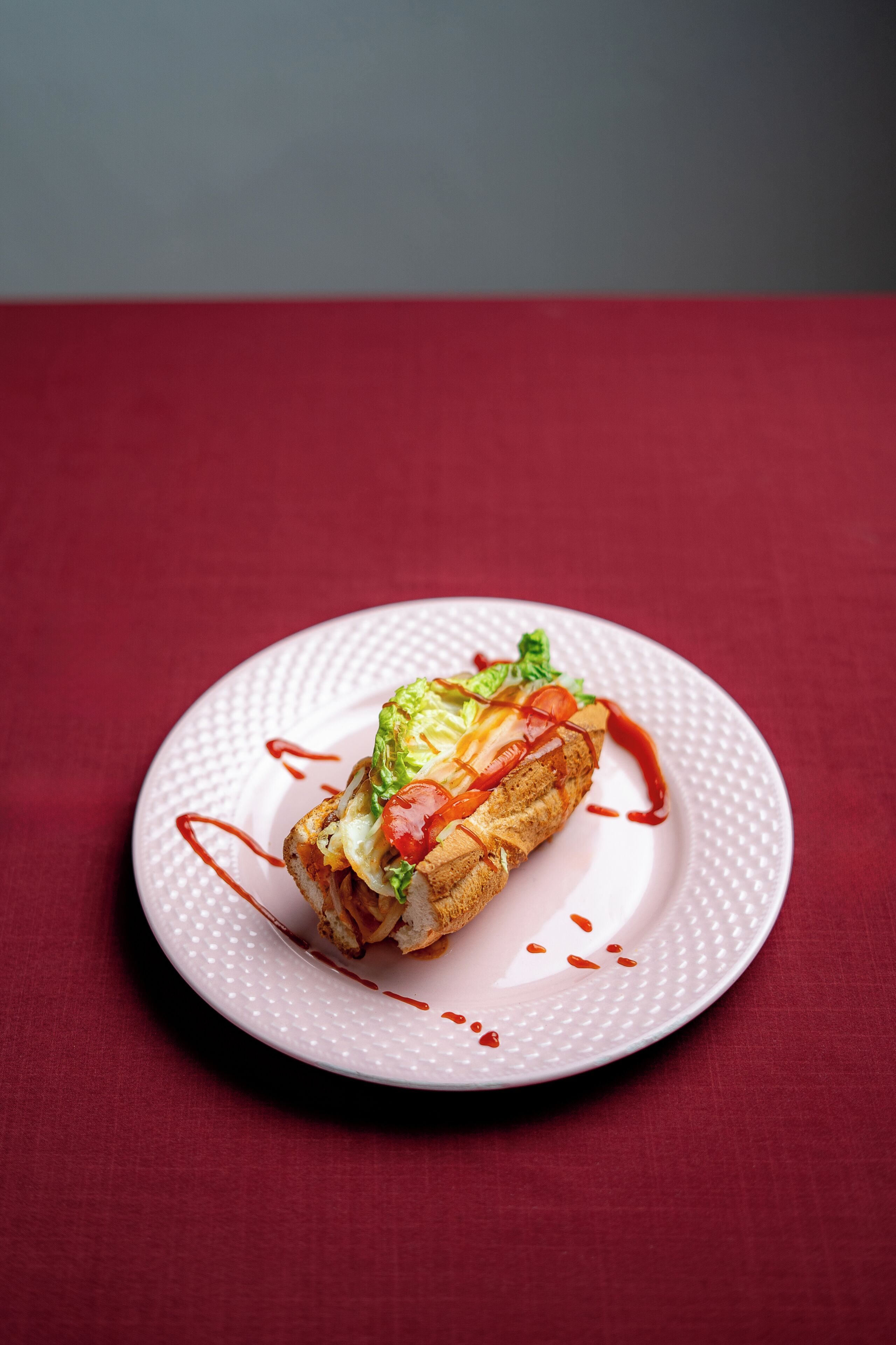 A sandwich on a white plate with a red background.