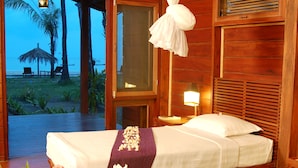 Un dormitorio de madera con una cama, mesita de noche y vista a la playa.