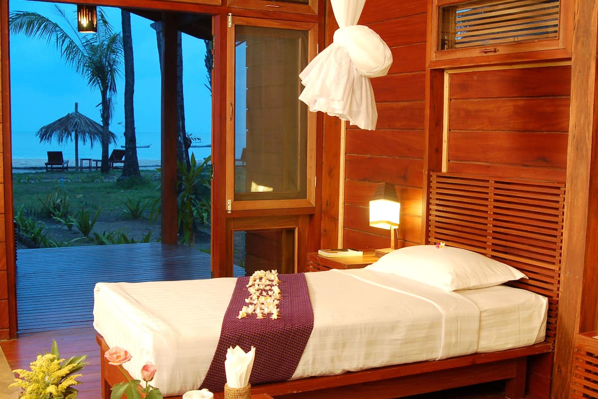 Ein Schlafzimmer aus Holz mit Bett, Nachttisch und Blick auf den Strand.