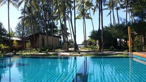 Una piscina con agua azul cristalina, rodeada de palmeras y un edificio con tejado de baldosas.
