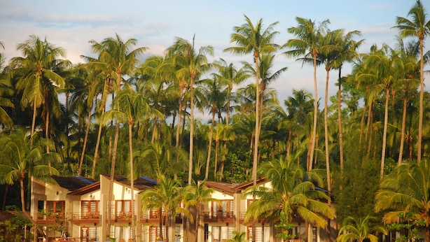 Un hotel frente a la playa con varios balcones, palmeras y sillas de playa.