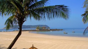 Una playa con una palmera, una sombrilla de paja y dos sillas de playa.