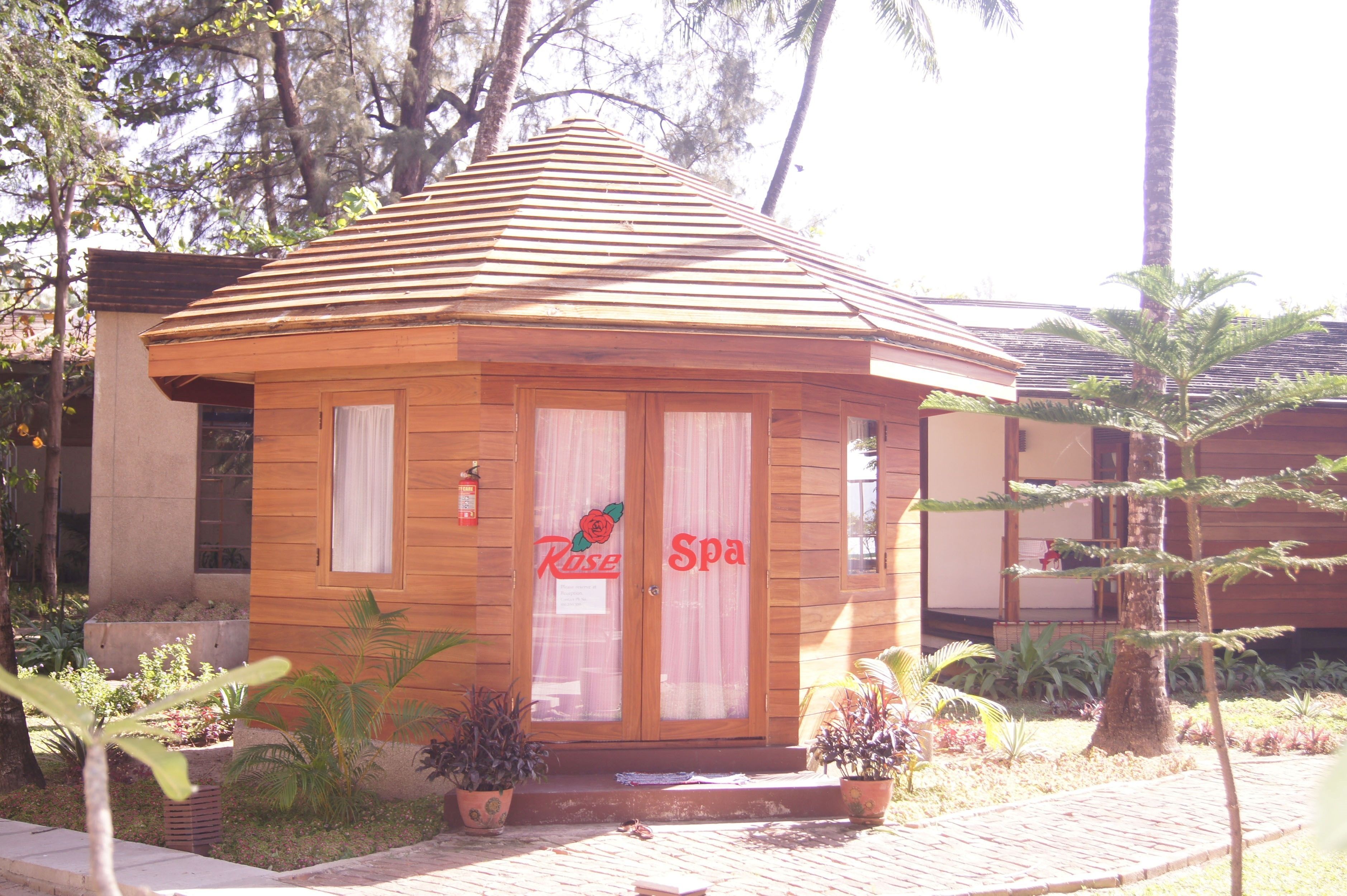 A wooden spa building with a sloped roof, two glass doors with a rose logo, and a sign reading "Rose Spa".