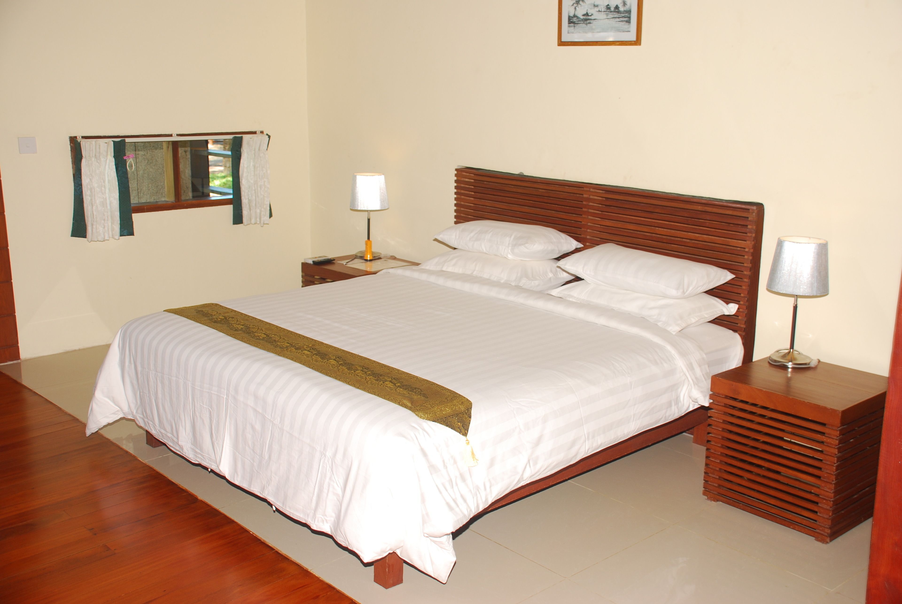 A neatly made bed with a wooden headboard, a bedside table with a lamp, and a window with curtains.