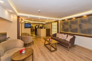 A modern hotel lobby with a reception desk, seating area, and a large decorative wall.