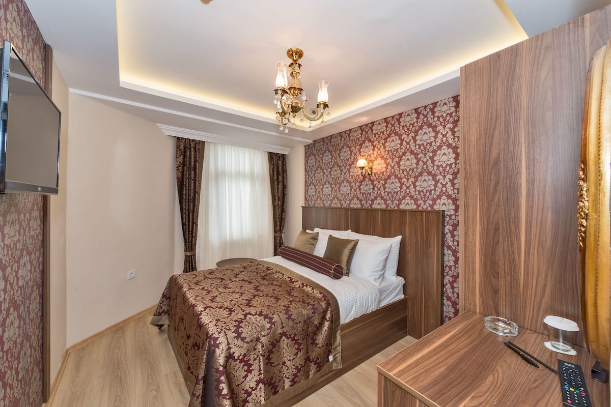 A hotel room with a bed, bedside table, and a television mounted on the wall.