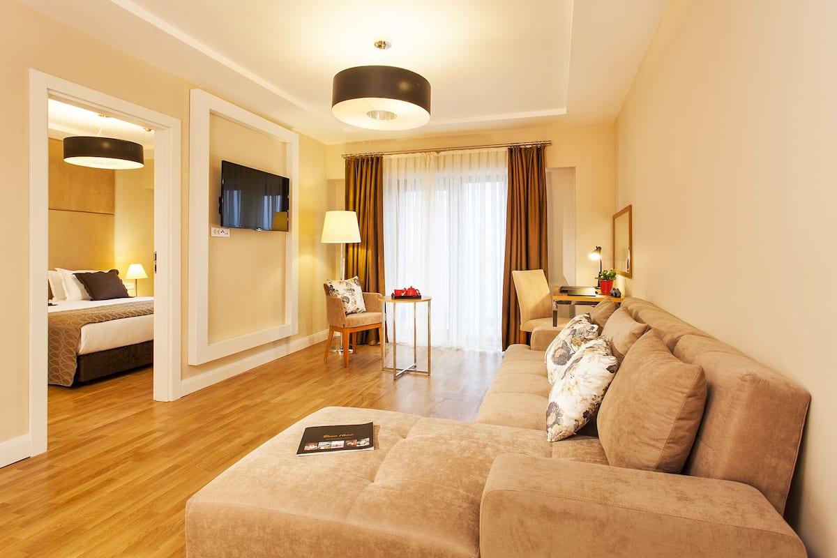 A hotel room with a sofa, a chair, a small table, a TV, and a lamp.