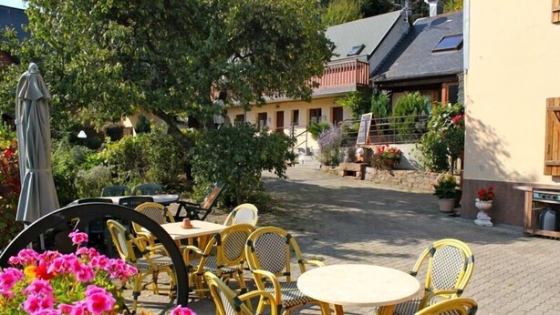 An outdoor patio area with wicker chairs and tables, surrounded by potted plants and flowers. - Domaine de Basil (Orbey)
