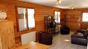 A wooden cabin interior with a dining table, leather sofa, and a small dining table with chairs. - Domaine de Basil (Orbey)