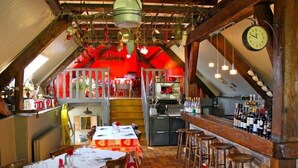 A restaurant with a red interior, wooden beams, a bar area with stools, and a kitchen visible in the background. - Domaine de Basil (Orbey)