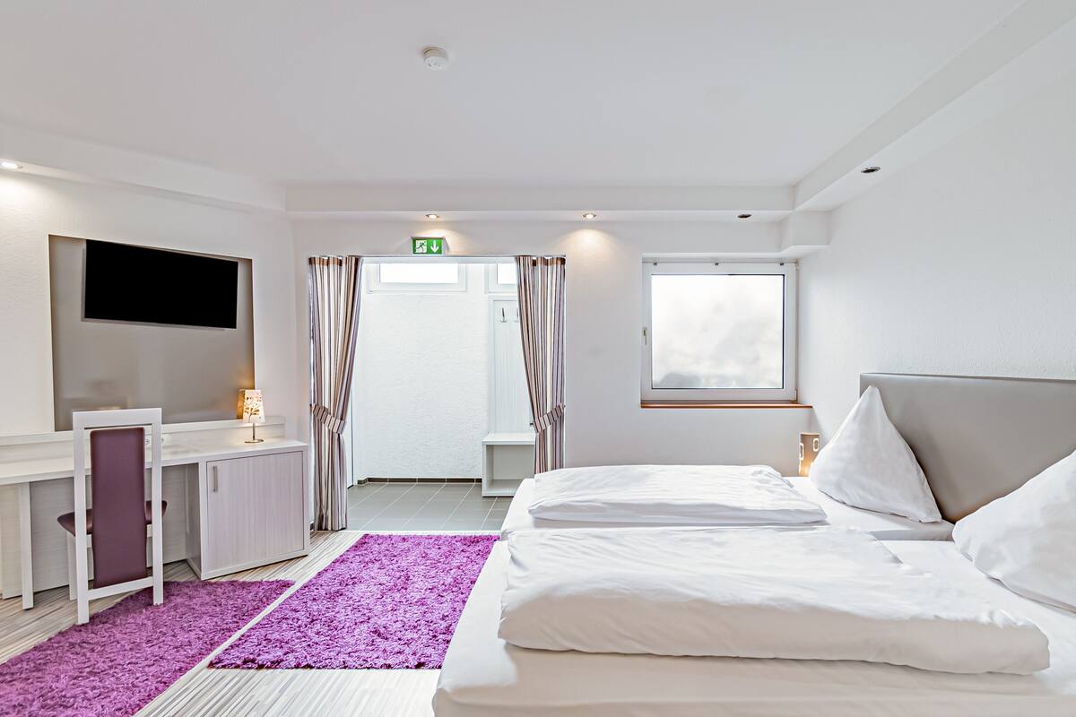 A hotel room with a bed, a desk, a TV, a window, and a bathroom door.