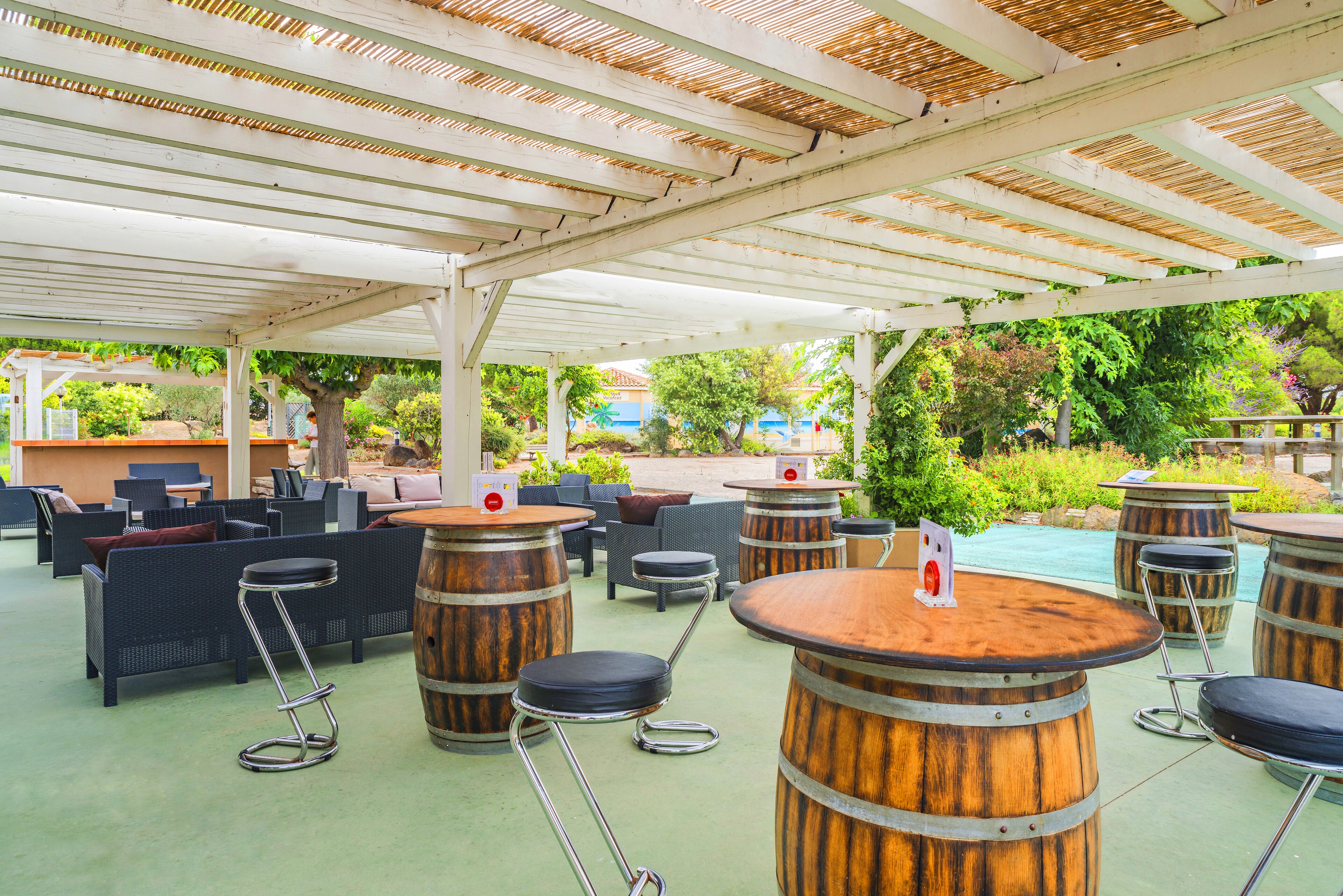 Un espace extérieur aménagé en terrasse, avec des tabourets en forme de tonneaux en bois, des meubles en osier et une piscine en arrière-plan.