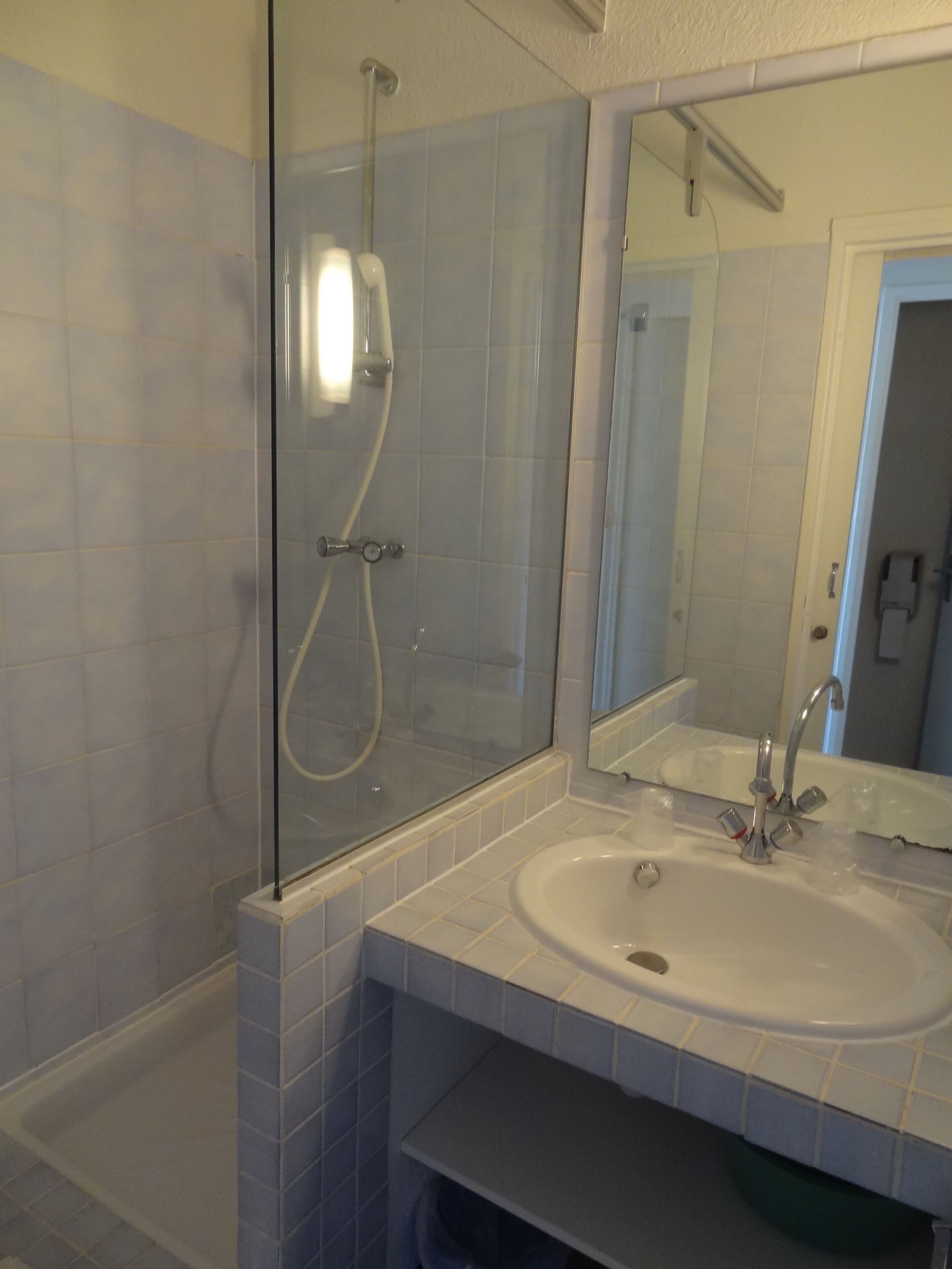 A bathroom with a glass-enclosed shower, a sink with a mirror above it, and a door leading to another room.