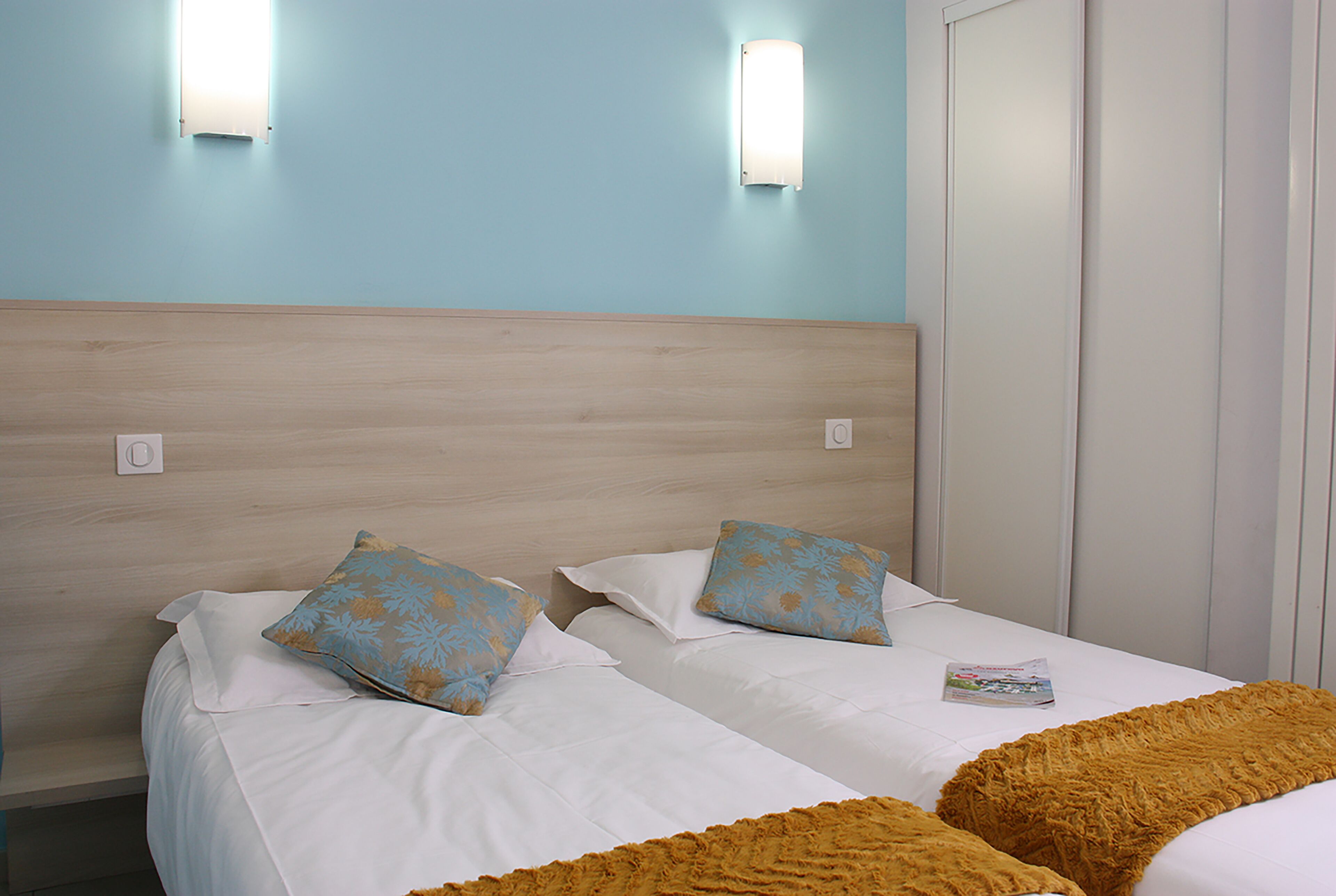 Een hotelkamer met twee bedden, lichtblauwe wanden en een houten hoofdbord.
