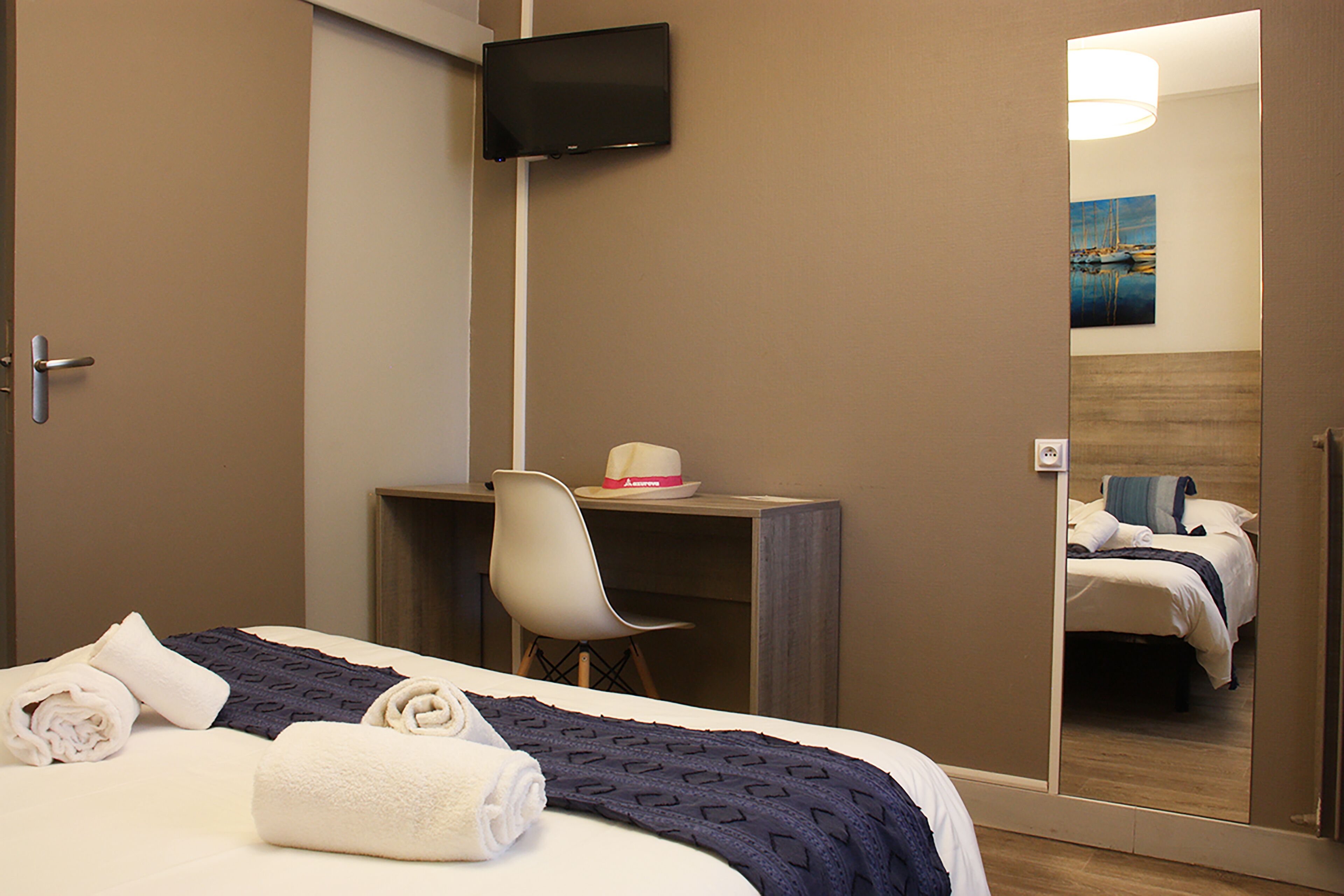 Una habitación de hotel con cama, escritorio, silla, televisor y espejo.