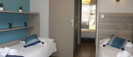 A hotel room with two beds, a door leading to a balcony, and a small shelf with plants.