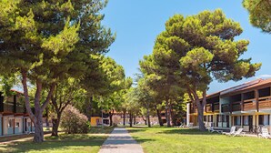 A pathway lined with trees leading to a building with multiple balconies and outdoor seating areas.