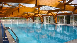 An indoor swimming pool with clear blue water, wooden beams, and large windows.