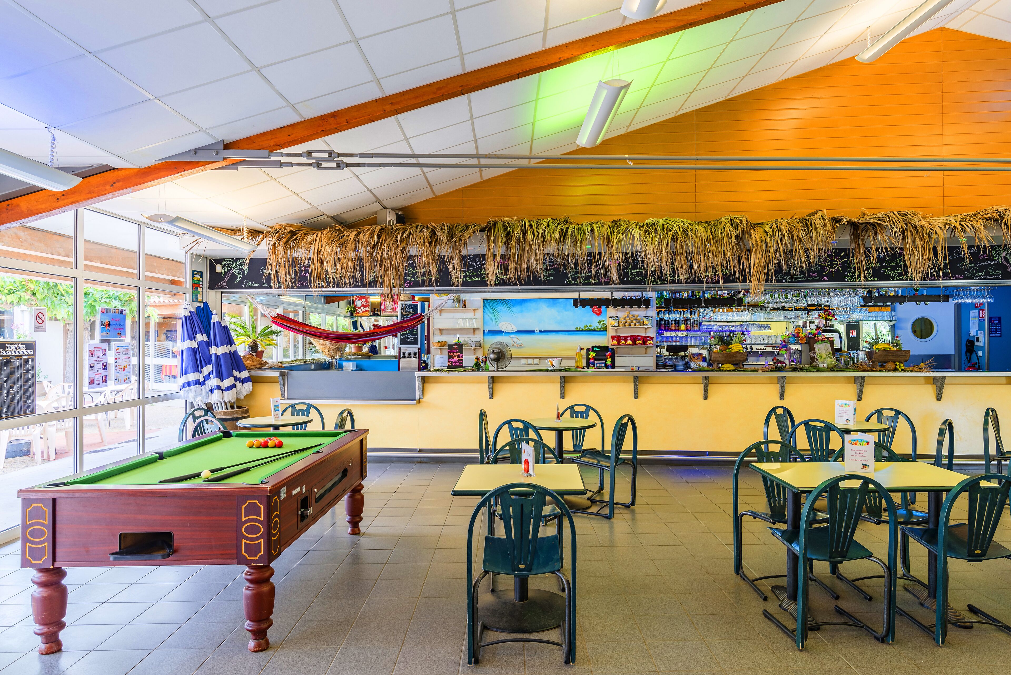 A pool table, chairs, and a bar area with a tropical theme.