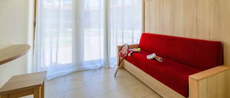 Ein Zimmer mit einer roten Couch, einem Holz-Fernsehschrank und einem Tennisracket auf dem Boden.