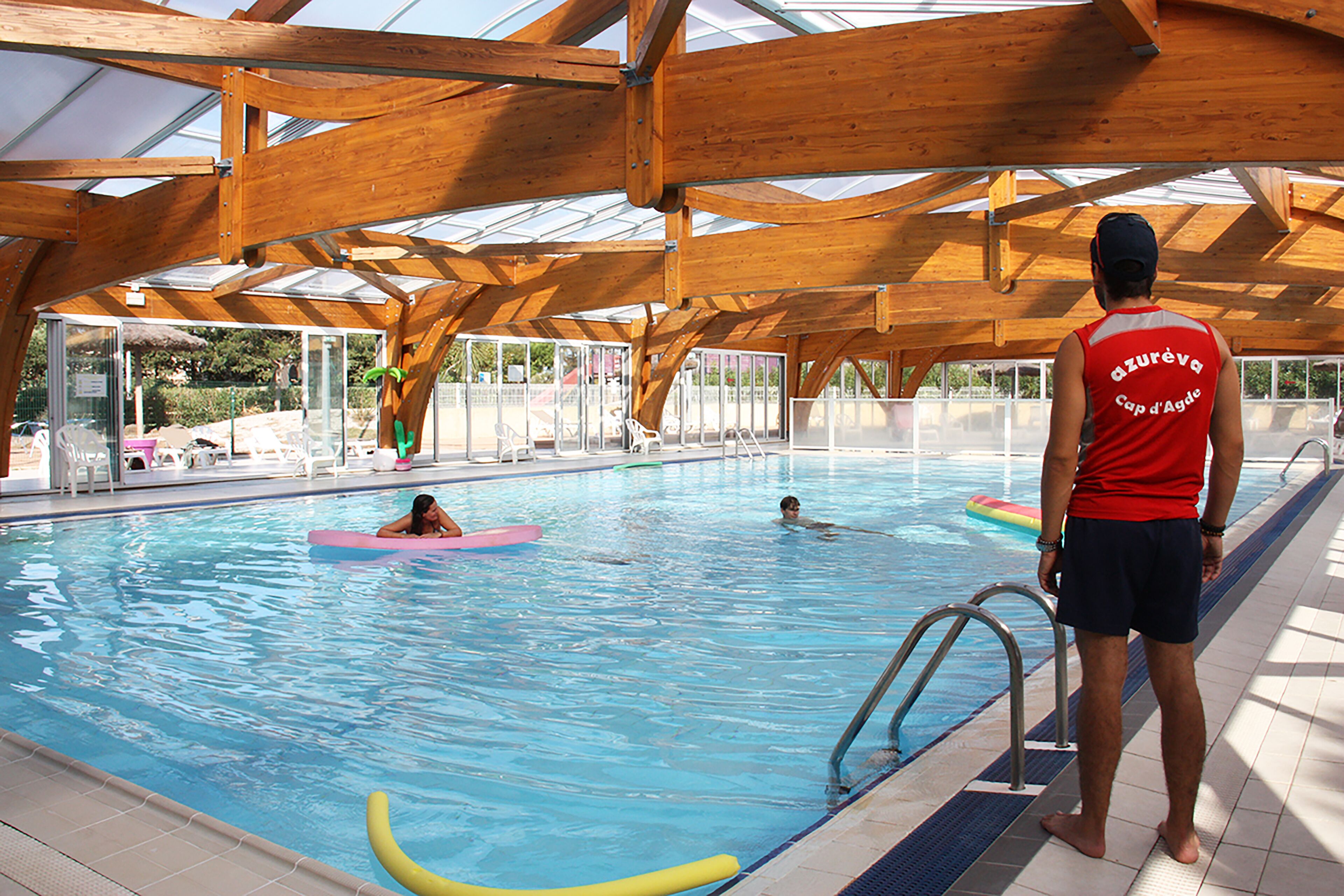 An indoor swimming pool with wooden beams and glass panels.