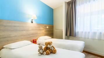 A hotel room with two beds, a wooden headboard, a nightstand with a lamp, and a window with curtains.