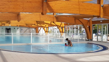 Ein großer, überdachter Pool mit Holzbalken, Glaswänden und Fliesenböden.