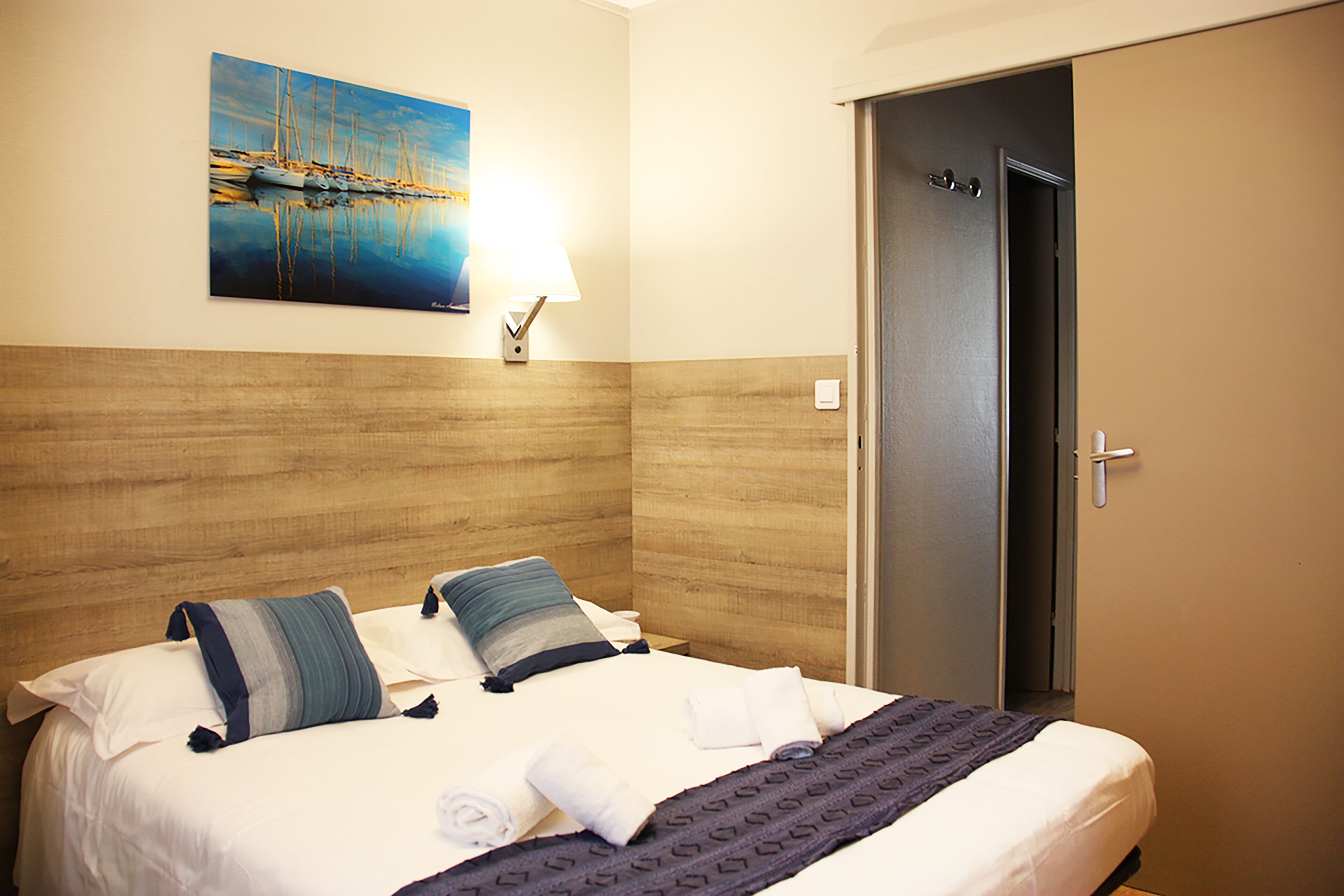 Ein Hotelzimmer mit Bett, Kissen, einem Gemälde, einem Nachttisch und einer Tür.