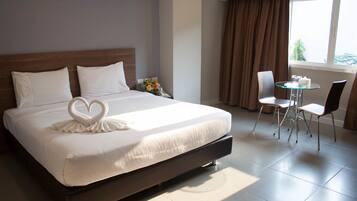 A hotel room with a large bed, a small table with chairs, and a window with curtains.