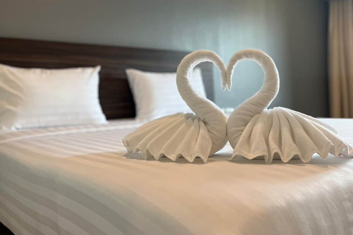 Una habitación de hotel con una cama bien hecha, una toalla dispuesta en forma de corazón y una pared lisa.