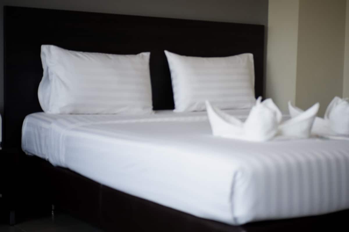 Una cama bien tendida con sábanas y almohadas blancas, un cabecero oscuro y una mesita de noche sencilla.