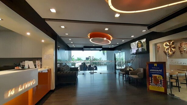 A modern hotel lobby with a reception desk, seating area, and a large window offering a view of the street. - 14 Living (Bangkok)