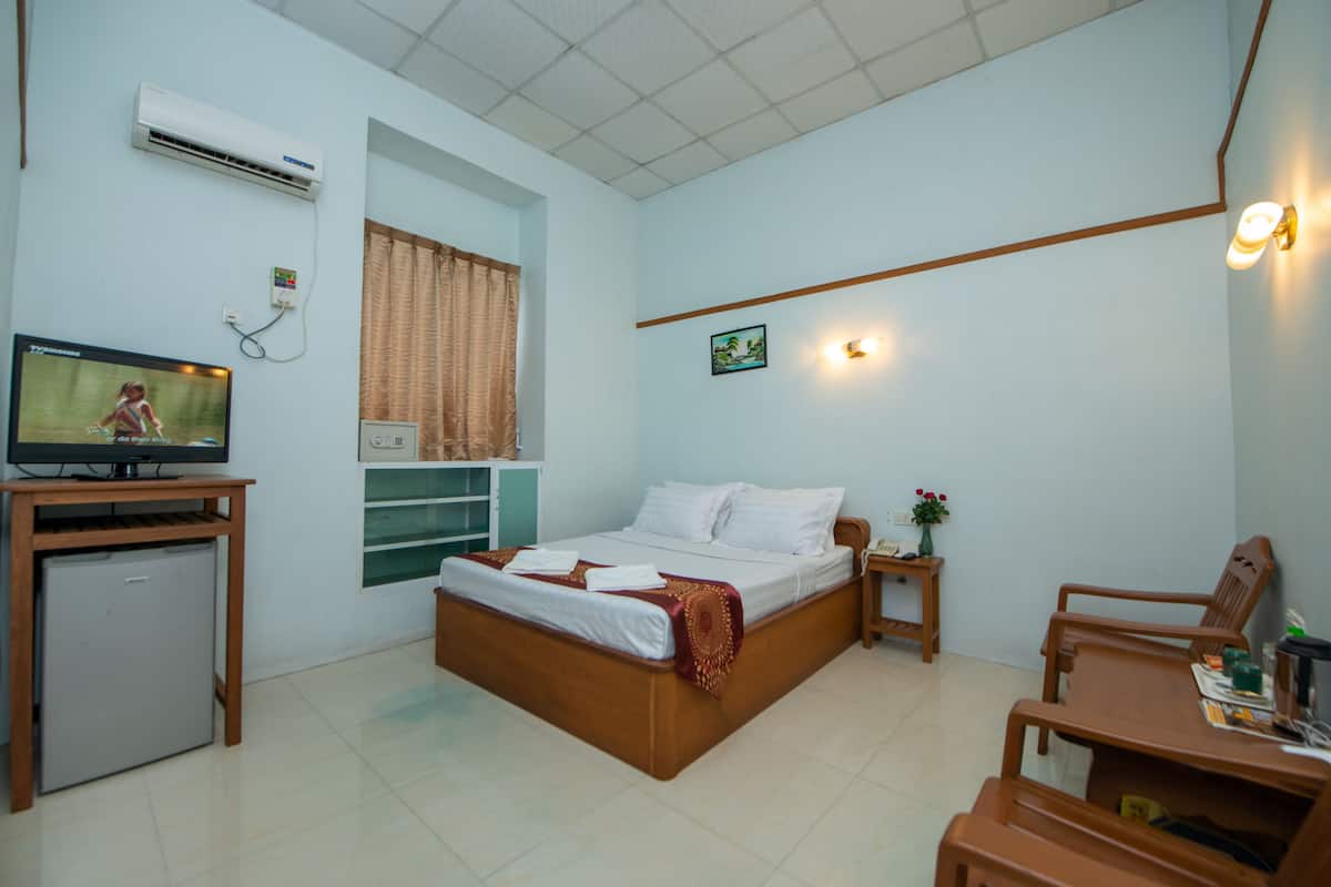 A bedroom with a bed, a desk, a TV, an air conditioner, and a small fridge.