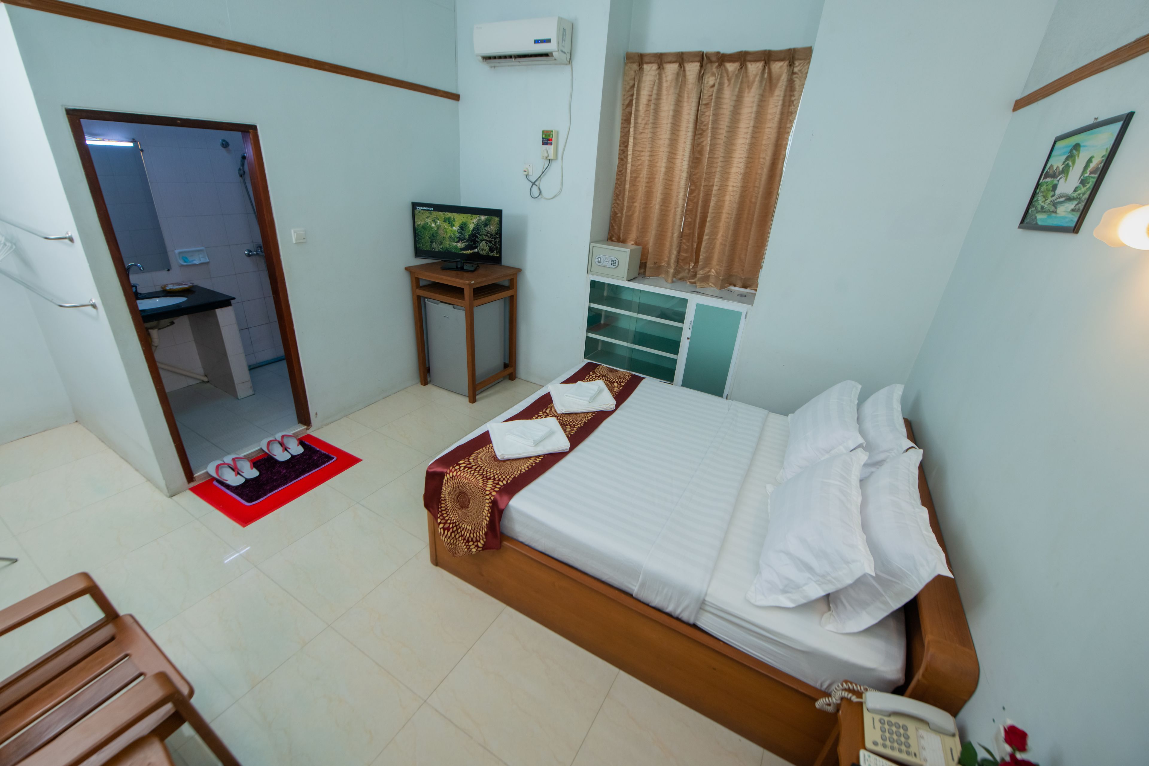 A hotel room with a bed, a small table with a TV, a bathroom visible through an open door, and a telephone on the bedside table.