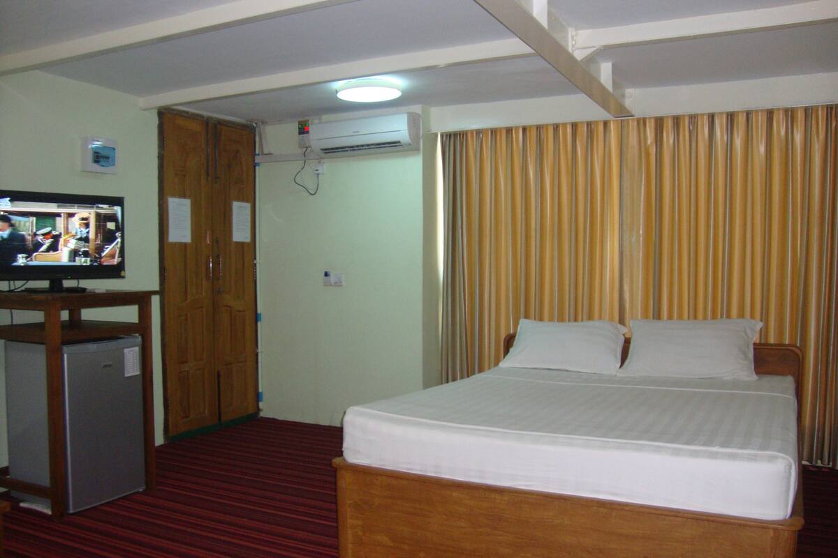 A hotel room with a bed, a television on a stand, and a small refrigerator.