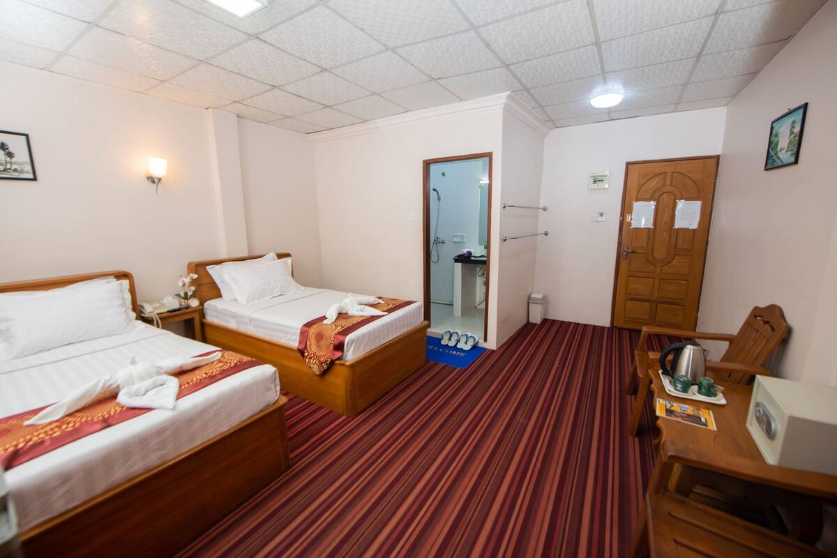 A hotel room with two beds, a wooden desk, a chair, a mirror, and a door.