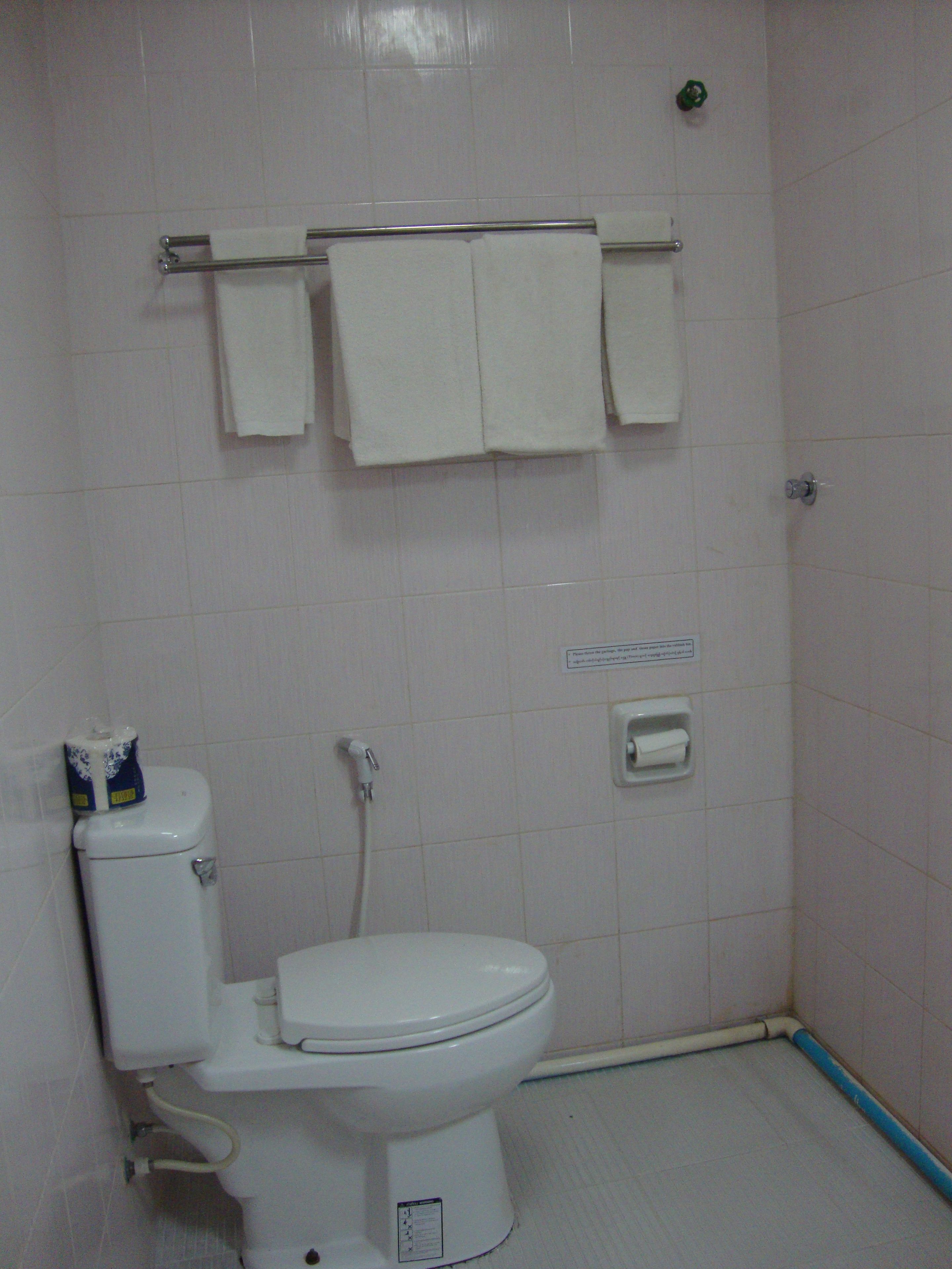A small, clean bathroom with a toilet, a towel rack with two towels, a toilet paper holder, and a sign on the wall.