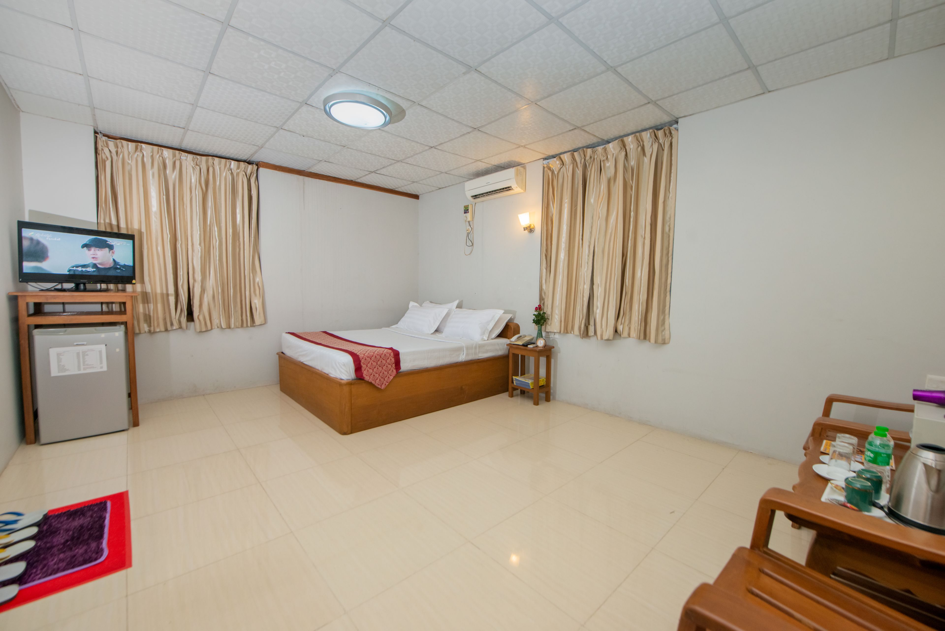 A hotel room with a bed, a television, a desk, and a small refrigerator.