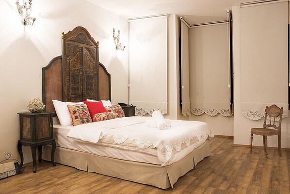 A neatly made bed with a wooden headboard, a small bedside table, and a chair in a room with wooden flooring and white walls. - Oriella Hotel (Istanbul)