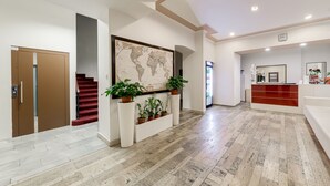 A modern lobby with a marble floor, a reception desk, a world map artwork, and potted plants. - Hotel Koruna (Prague)