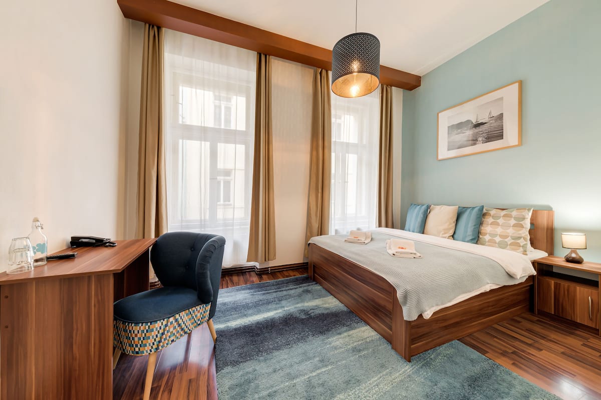 A modern hotel room with a wooden desk, a comfortable chair, a large bed with a blue and white striped bedspread, and a hanging light fixture.