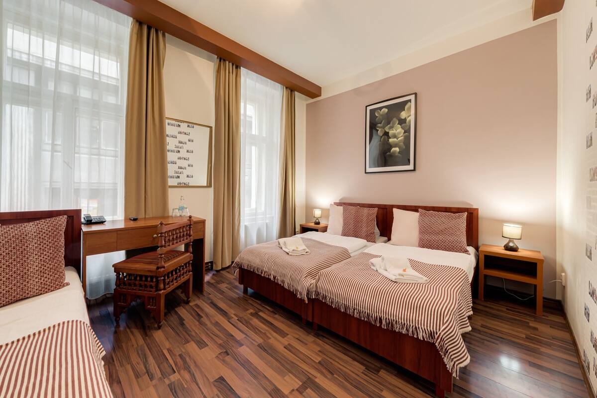 A hotel room with a wooden bed, a desk, a chair, and a nightstand with a lamp.