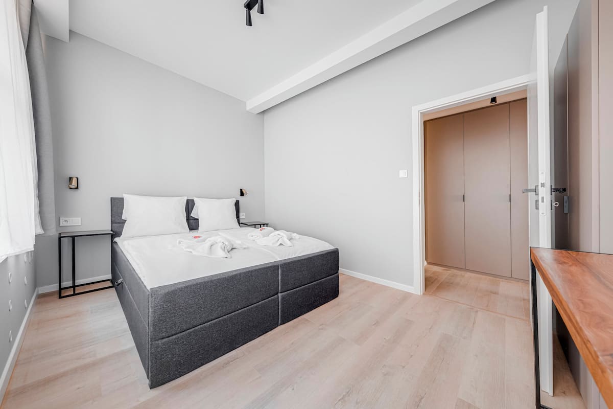 A modern bedroom with a grey bed, a wooden nightstand, and a wardrobe.